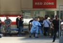 A group of people, including medical staff and other individuals, standing outside an emergency hospital entrance marked "Red Zone."