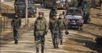 Group of soldiers patrolling a rural road with military vehicles in the background.