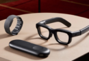 Modern smart glasses with a wrist strap and a sleek casing on a table.